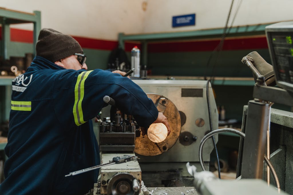 Industrial worker focused on operating a lathe in a busy workshop setting.